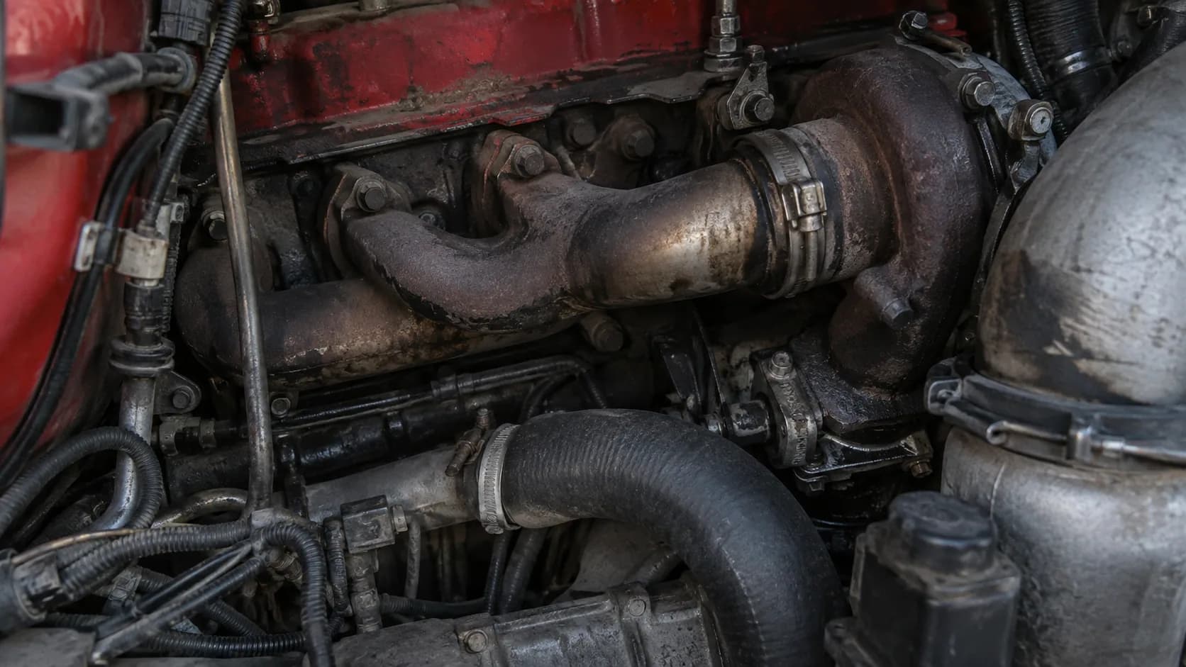 Up close on the exhaust manifold, turbo and hoses of a grimy red engine. The kind of detail only a mechanic or a Mack fan can love.