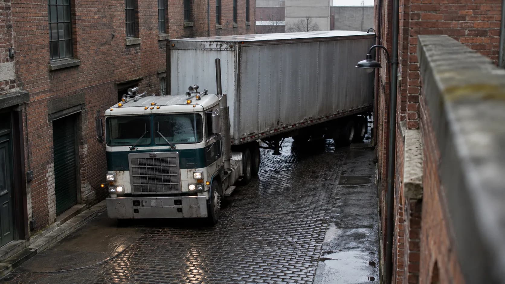 A cabover easing a long trailer down a wet brick alley with barely room to spare. This is where the flat nose earned its keep.