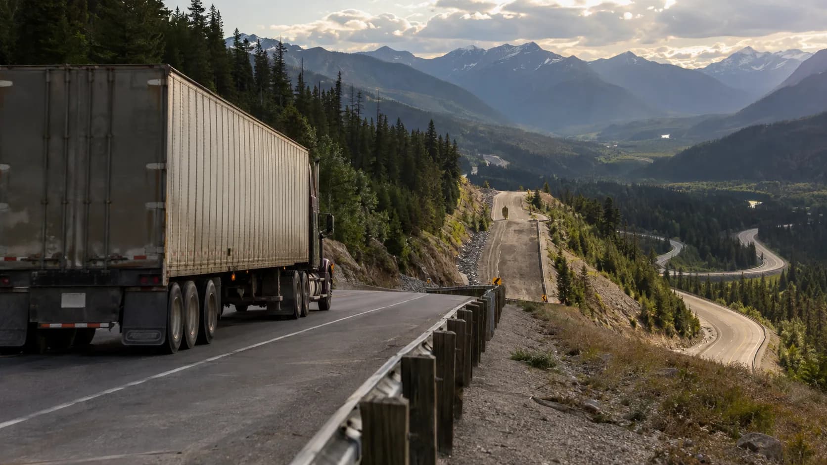 AI-generated render of a box-trailer semi truck heading down a mountain highway with evergreen forest and a winding road in the valley below